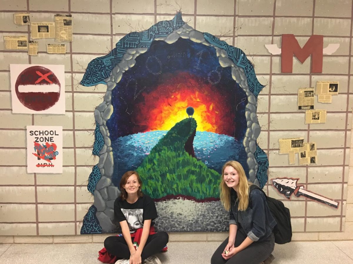 Seniors Caitlin Simons and Emma Minett were part of a team that created the 2018 Senior Mural.  It was hung on a block wall — that it was designed to match — at Central Campus on Sept. 28.