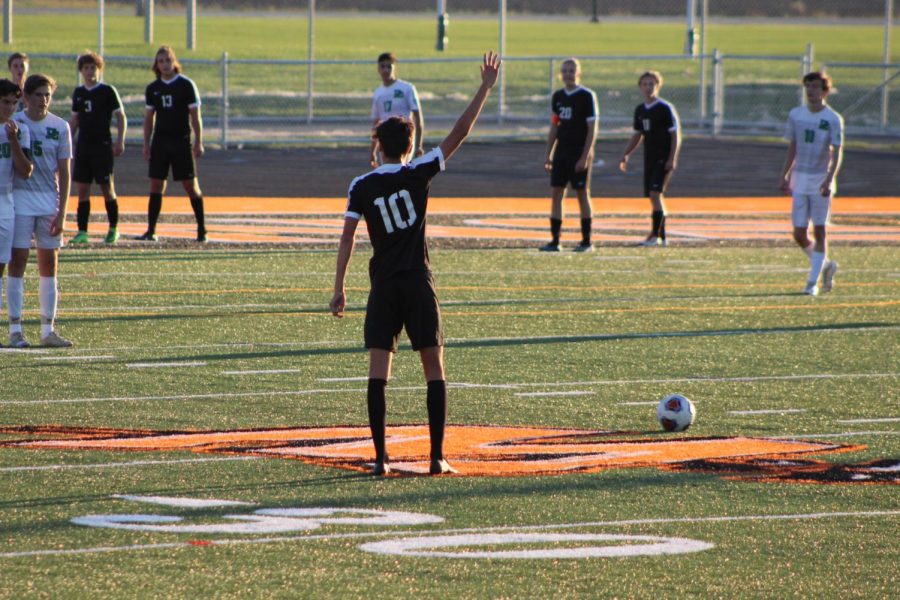 Izaak Avalos, senior, takes a free kick. With his arm up, he signals he is not moving yet. Once the referee blows his whistle Avalos can continue and follow through with a power kick to put the ball into play for his teammates.