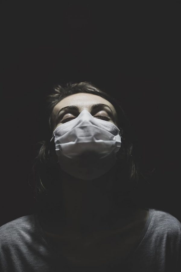 A woman is wearing a mask to protect herself from the virus, but appears to be alone and surrounded by the dark. Numerous medical agencies stress the importance of monitoring mental health, especially during tough times like these. 